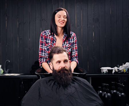 Brunette female hairdresser washing the hair of the bearded men client in a saloon.の写真素材