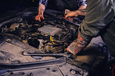 Close up image of two mechanics with tattoos on arms, fixing car's engine parts in a workshop.の写真素材