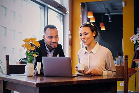 Black African American business male and female drinks coffee and using a laptop in a restaurant.のeditorial素材