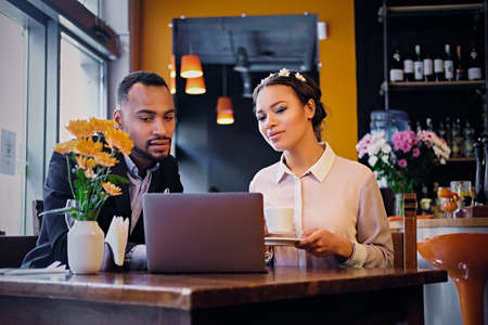 Black African American business male and female drinks coffee and using a laptop in a restaurant.のeditorial素材