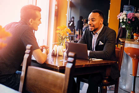Caucasian and black American men talks and using a laptop in a restaurant.のeditorial素材