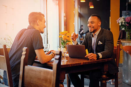 Caucasian and black American men talks and using a laptop in a restaurant.のeditorial素材