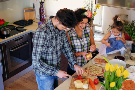 Happy family of brunette female, handsome male in a fleece shirt and cute little girl cooking food in a home kitchen.の写真素材