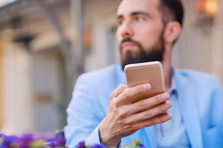 Stylish bearded male in a blue jacket using smartphone.の写真素材