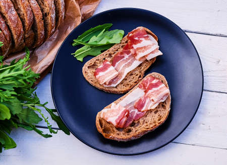 Bread with ham and herbs on a black plate on a wooden table.の写真素材