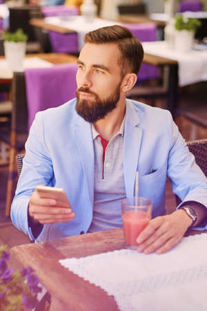 Stylish bearded male in a blue jacket using smart phone in a cafe.
