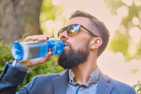 Bearded hipster male in sunglasses, drinks mineral water.の写真素材