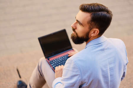 The stylish bearded male sits on a step and using laptop.の写真素材