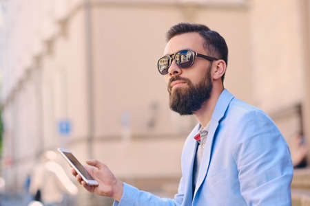 Portrait of bearded male in sunglasses using a smartphone.の写真素材