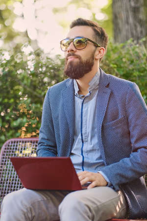 Handsome bearded male using laptop in a park.の写真素材