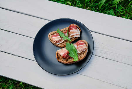 Bread with ham and herbs on a black plate on a wooden table.の写真素材