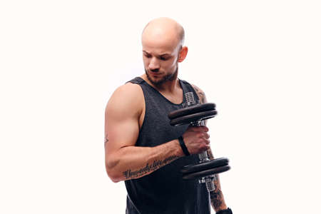 Portrait of athletic shaved head male with tattoos on arm holds dumbbell. Isolated on a white background.の写真素材