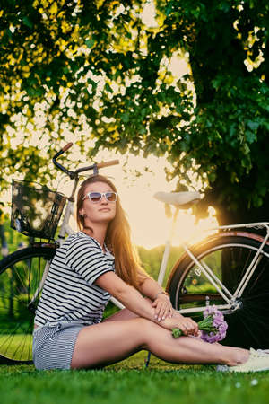 Portrait of brunette female sits on a lawn in a sunny park.の写真素材
