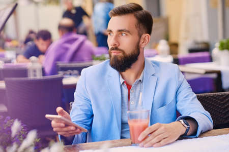 Stylish bearded male in a blue jacket using smart phone in a cafe.の写真素材
