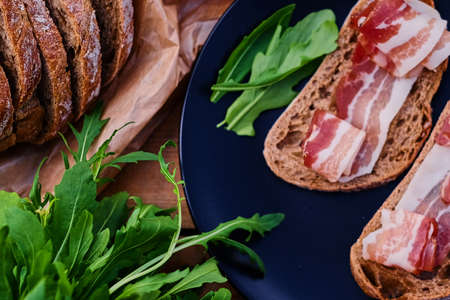 Bread with ham and herbs on a black plate on a wooden table.の写真素材