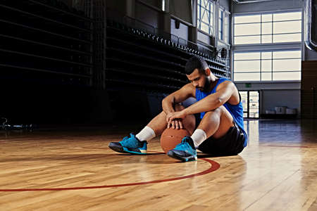 Black professional basketball player sits on a floor in a game hall.の写真素材
