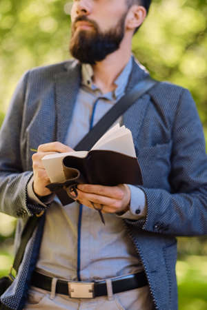 Stylish bearded male writing a message to a notepad in a park.の写真素材