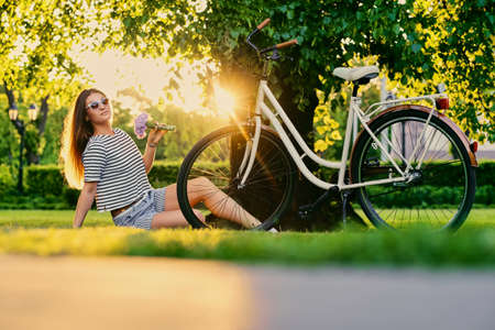 Portrait of brunette female sits on a lawn in a sunny park.の写真素材