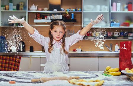 Cheerful little girl cooking dough at the kitchen.の写真素材