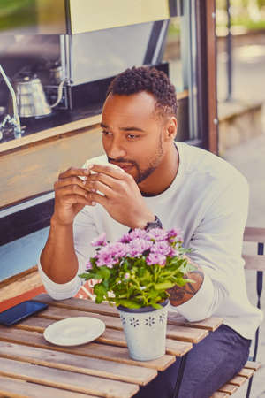 Black man drinks coffee in a cafe on a street.の写真素材