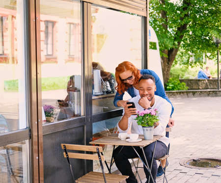 Black bearded male and redhead female drink coffee in a cafe on a street.の写真素材