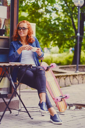 Redhead female drinks coffee after skating on Longboard.の写真素材
