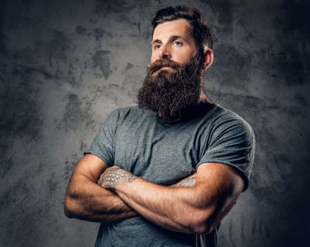 Brutal bearded male with tattoos on arms over grey background.の写真素材