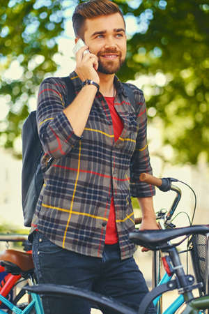 A positive bearded male dressed in a fleece shirt using a smart phone near bicycle parking.