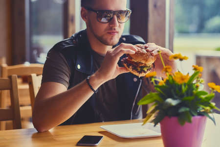 Attractive hipster dressed in leather jacket eating a vegan burger.の写真素材