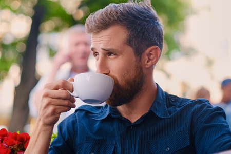 Portrait of bearded redhead casual man drinks coffee in a cafe on a street.の写真素材
