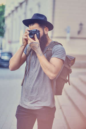 Portrait of casual tattooed, bearded street photographer taking pictures.