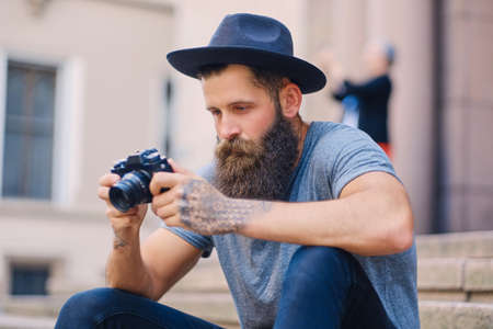 Portrait of casual tattooed, bearded street photographer sits on a step.の写真素材