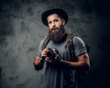 Studio portrait of bearded tattooed photographer holds compact camera over grey background.の写真素材