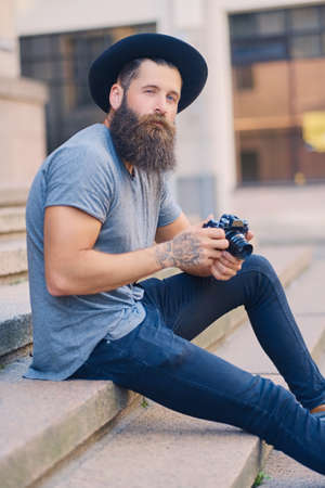 Portrait of casual tattooed, bearded street photographer sits on a step.の写真素材