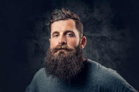 Brutal bearded male with tattooed arms over dark grey background.の写真素材