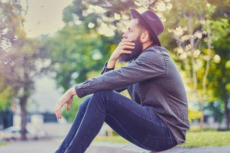 Casual bearded hipster sits on a step over city park background.の写真素材