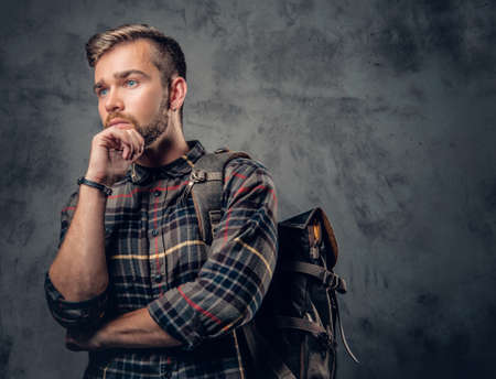 A bearded traveler male dressed in a fleece shirt with backpack posing over grey background.の写真素材