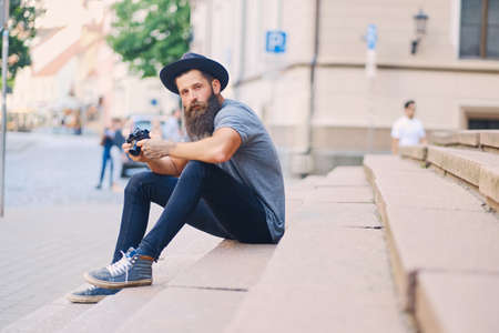 Portrait of casual tattooed, bearded street photographer sits on a step.の写真素材
