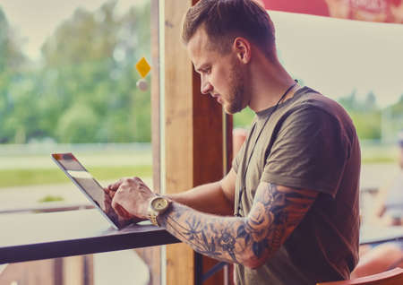 Stylish male with tattooed arms using smartphone in a cafe near window.の写真素材