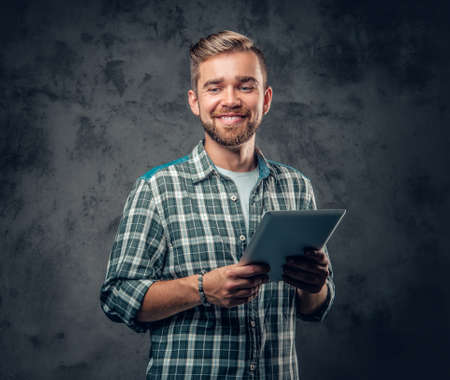 Bearded male in a fleece shirt holds tablet PC over grey background.の写真素材