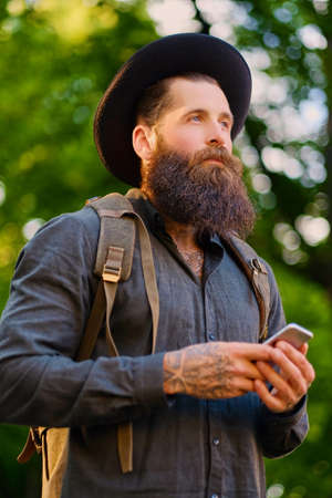 Bearded tattooed traveller male using a smartphone in a park.の写真素材