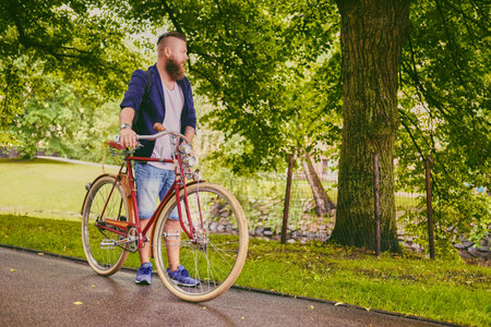 Redhead bearded hipster male on a retro bicycle in a summer park.の写真素材