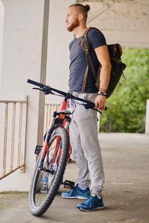 Sporty bearded male sits on a red mountain bicycle outdoor.