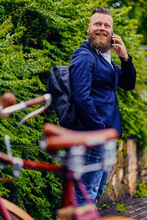 Casual bearded male in a park talks by smart phone.の写真素材