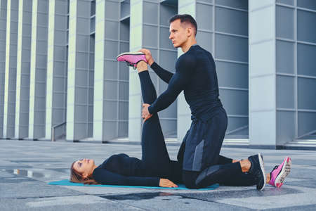 The athletic fitness couple is exercising on an aerobic mat over modern building background.