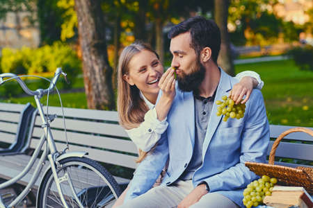 A couple eats grape on a bench in a park.の写真素材