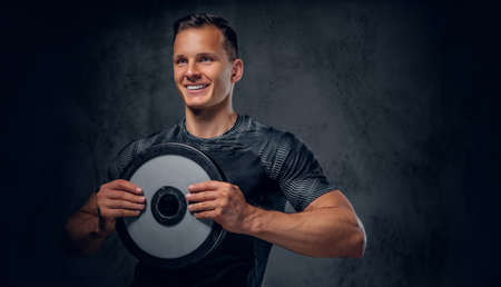 Athletic male holds a barbell weight in his arm over grey background.の写真素材
