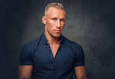 Handsome blond man in a dark blue shirt posing over grey background in a studio.の写真素材