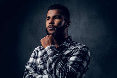 Thoughtful Black, bearded male with crossed arms over grey background.の写真素材