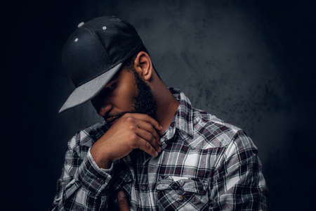 Thoughtful Black, bearded hipster male dressed in a fleece shirt and baseball cap.の写真素材